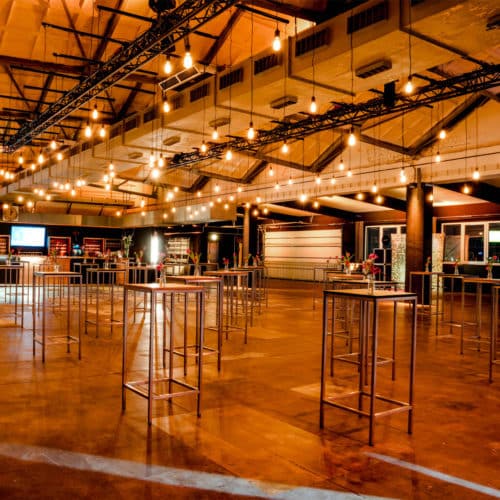 Als Eventagentur in Leipzig steht uns die Alte Wollkämmerei mit ihrem industriellen Charme für Ihr Event zur Verfügung. Hier warm ausgeleuchtet mit Edison-Glühbirnen und dekorativen Hochtischen mit Blick auf die Bar am Ende des Saals.