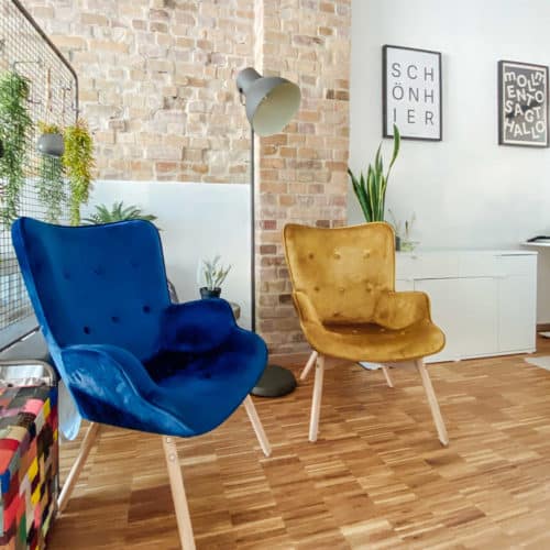 Ein Einblick in unser Büro. Zwei edle Sessel aus Samt vor einer einer hellen Backsteinwand mit zwei typografisch gestalteten Bilder.