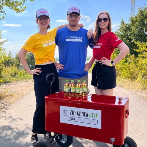Promotion ist ein wichtiger Bereich der Live Kommunikation. Zu sehen ist unsere fröhliche Truppe an Promotern, die in passend gebrandeten Shirts und Caps am Cospudener See Leipzig den Fruchtwein von Sachsenobst verteilen.