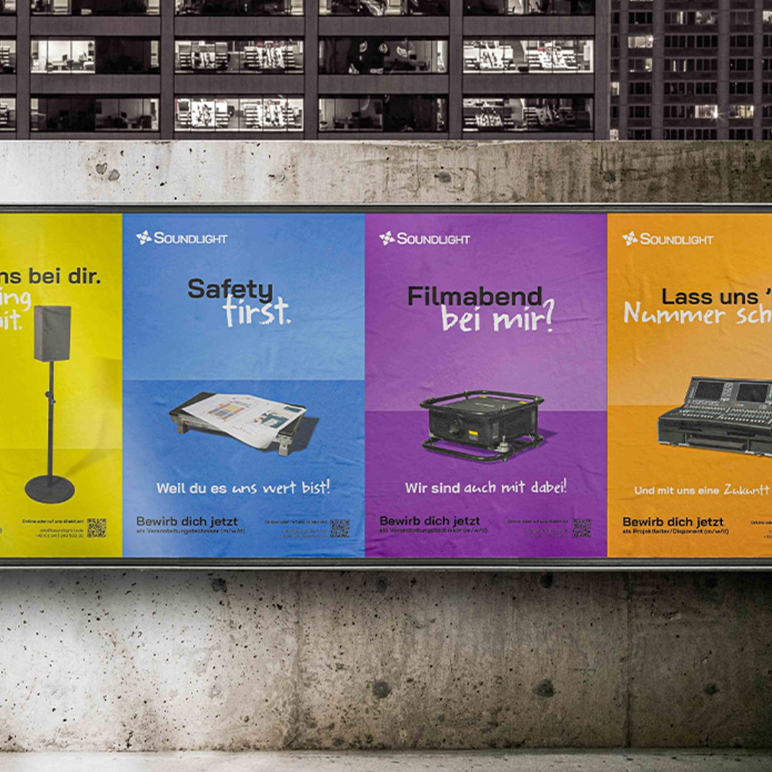 Blick auf eine raue Betonwand am Straßenrand. Dort in Reihe angebracht sind die verschieden farbigen Plakate der Marketing Kampagne zur Mitarbeitergewinnung unseres Kunden Soundlight.