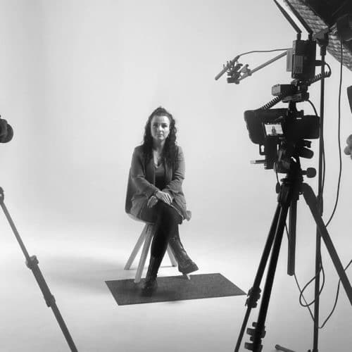 Schwarz-weiß Foto vom einer Interview-Situation. Eine Frau im Anzug sitzt auf einen Stuhl und schaut in die Kamera. Hinter den Kulissen einer Videoproduktion. Projekt: ZEIDLER GmbH Imagefilm.