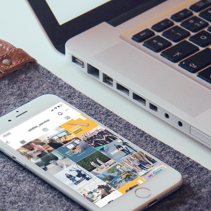 Neben einem im Anschnitt gezeigten Mac Book Pro liegt ein iPhone, auf dessen Display der Feed des Social Media Accounts unseres Kunden ZEIDLER GmbH zu sehen ist.